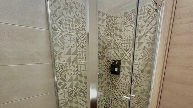 A shower with patterned tiles and a glass door. - B&b SunHouse (Napoli)