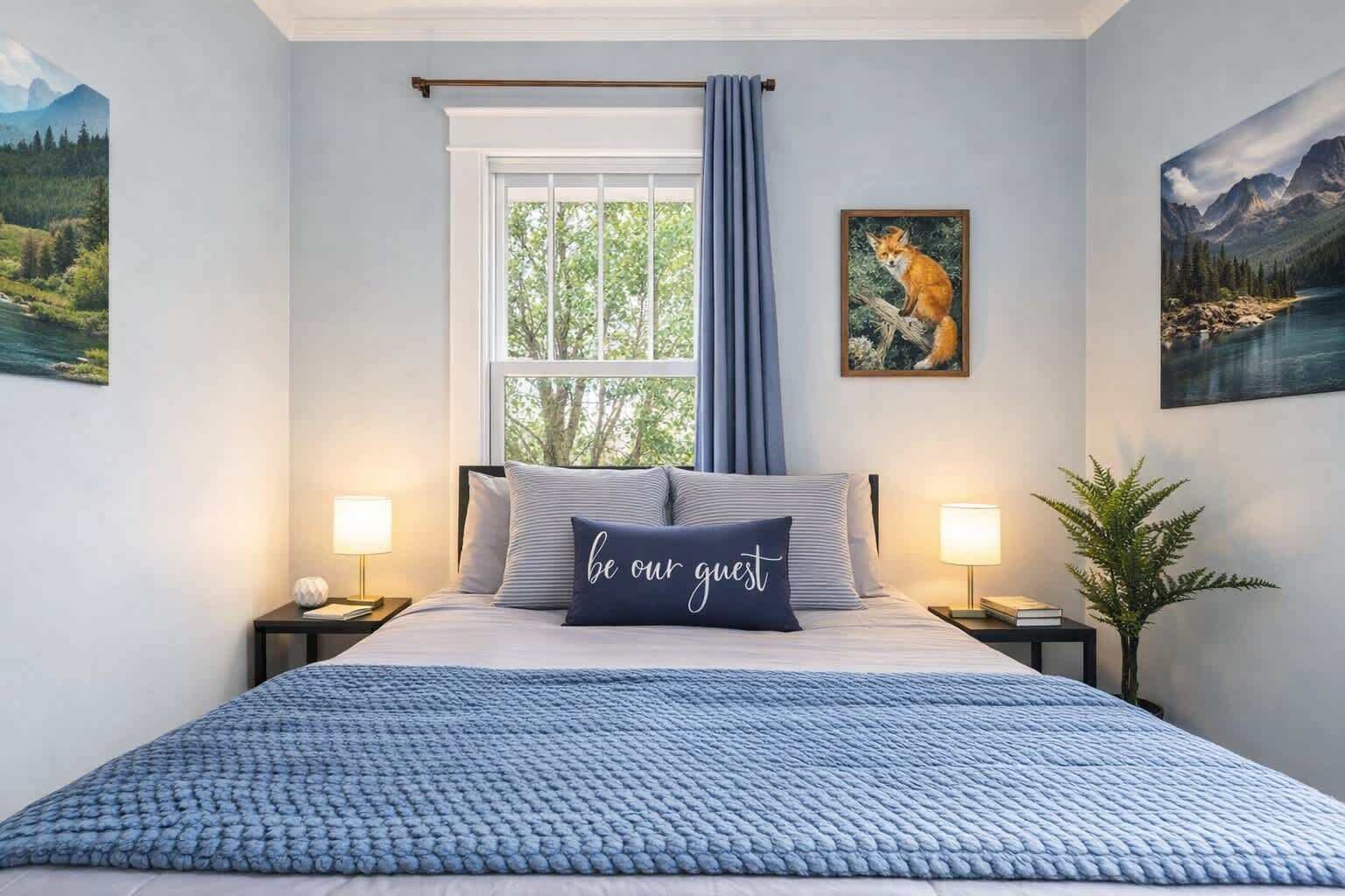 A bedroom with a bed, two bedside tables, a window with curtains, and wall art.
