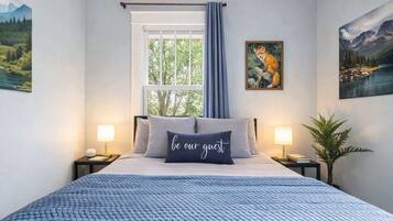 A bedroom with a bed, two bedside tables, a window with curtains, and wall art.