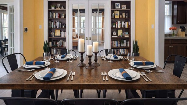 Comedor con una mesa de madera preparada para seis comensales, flanqueado por estanterías y vistas a otra habitación a través de una puerta de vidrio.