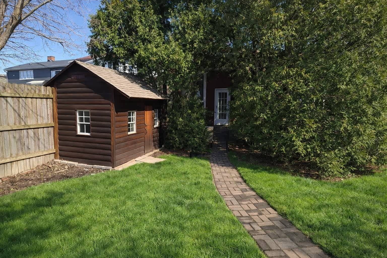 A wooden cabin with a brick pathway leading to it, surrounded by grass and trees.