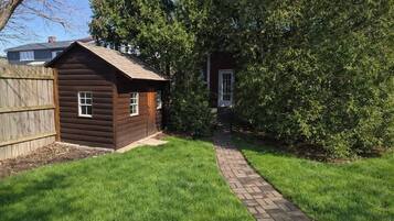 A wooden cabin with a brick pathway leading to it, surrounded by grass and trees.