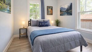 Un dormitorio con una cama, una mesita de noche, un ventanal y dos cuadros.