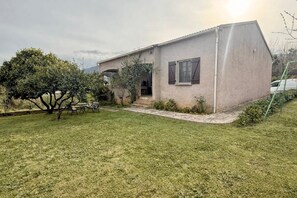 A single-story house with a small front yard, a bench, and a tree.