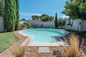 Ein rechteckiger Pool mit Kiesbordur, umgeben von einem gepflegten Rasen und verschiedenen Sträuchern.