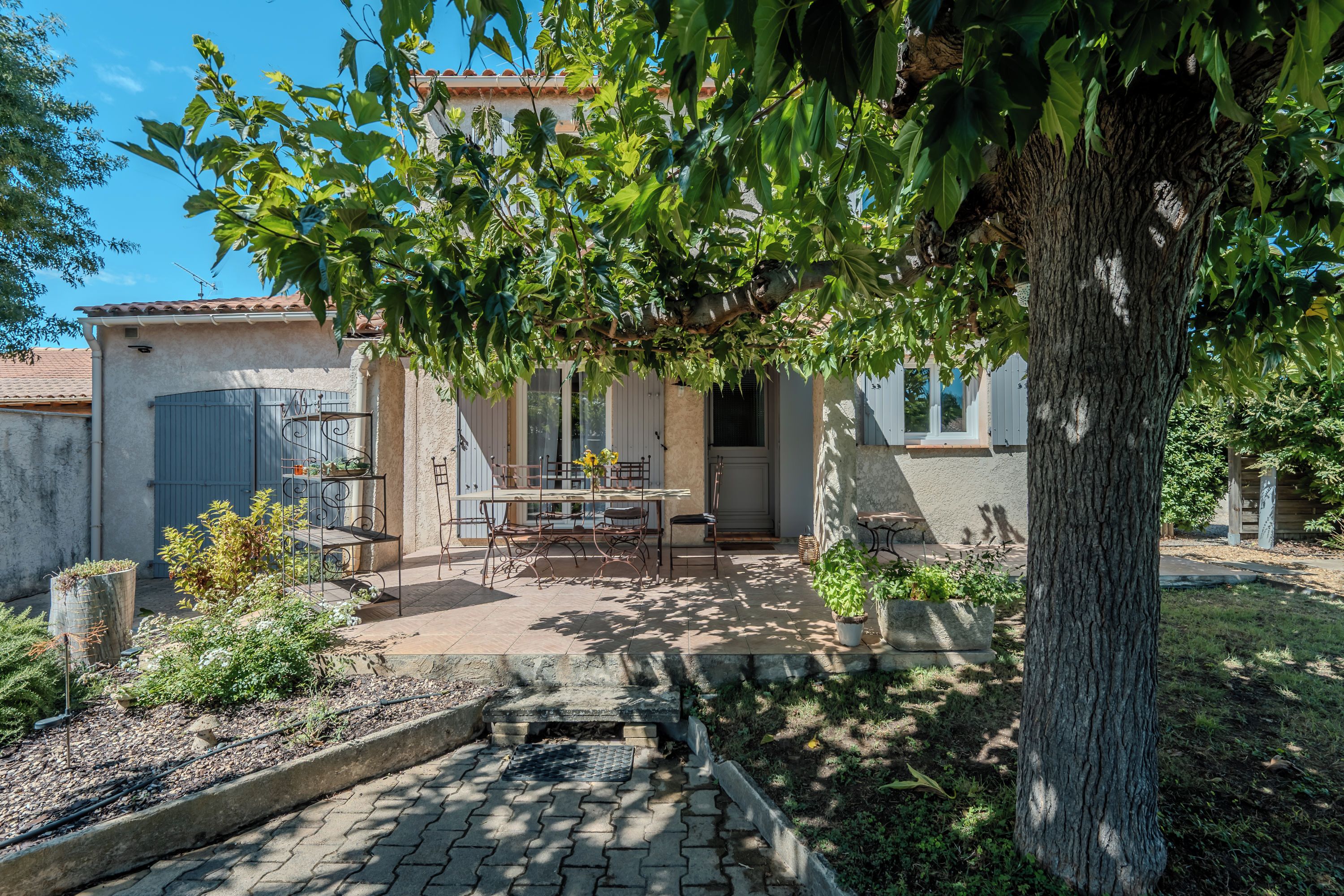 Une cour avec une table et des chaises, un petit jardin et un bâtiment doté d’un toit en tuiles.