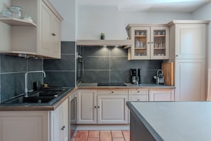 Een kleine keuken met een zwart fornuis, een koffiezetapparaat en kastjes met glazen deuren.