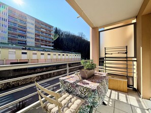 A balcony with a view of a train, a potted plant, a cushioned chair, and a small table. - T2 parking, prox thermes et centre-ville (Aix-les-Bains)