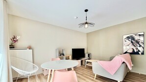 A modern living room with a round dining table, two chairs, a sofa, a TV, and a decorative ceiling light. - T2 parking, prox thermes et centre-ville (Aix-les-Bains)