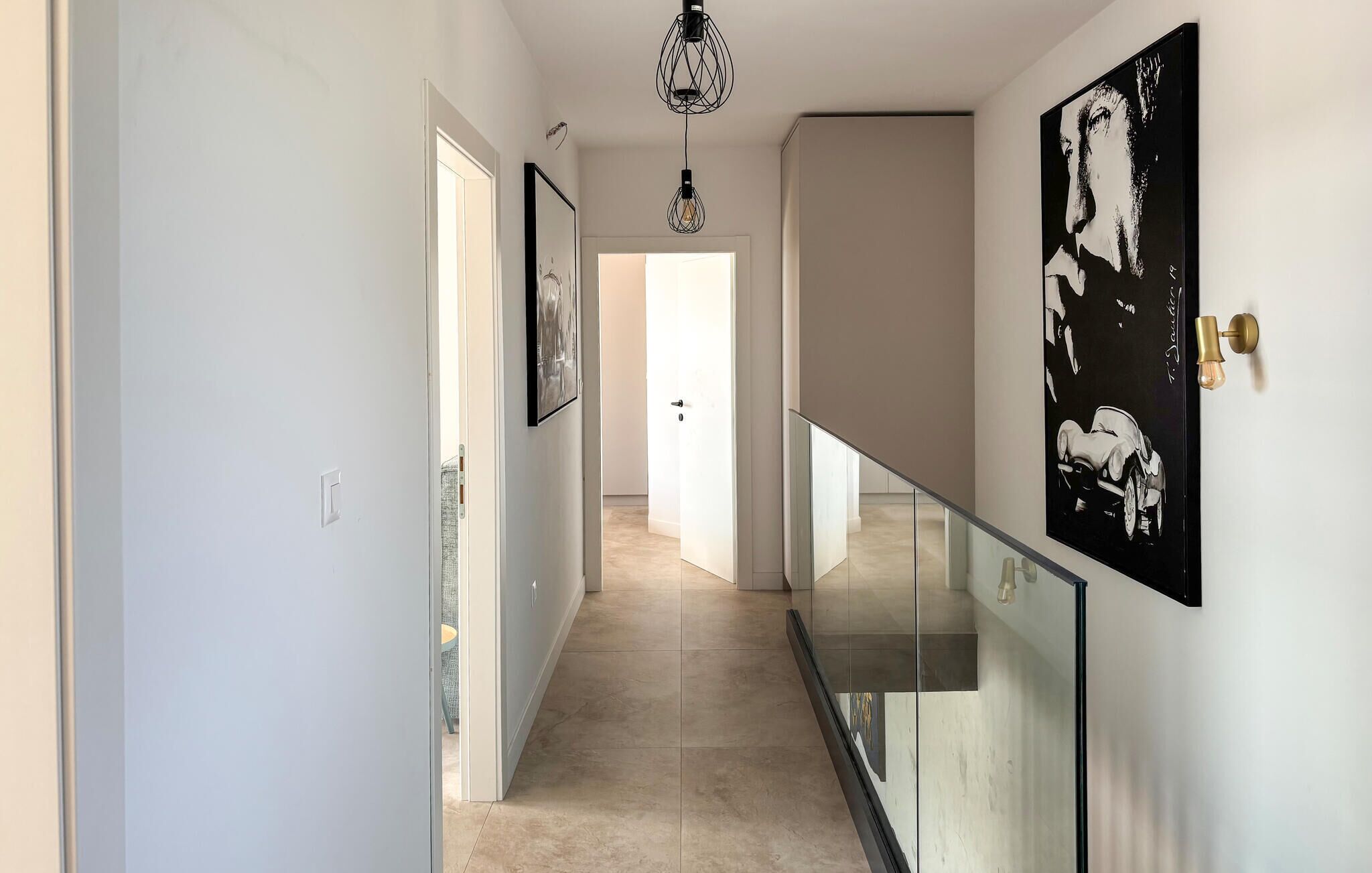 A hallway with a glass railing, a chandelier, and artwork on the walls.