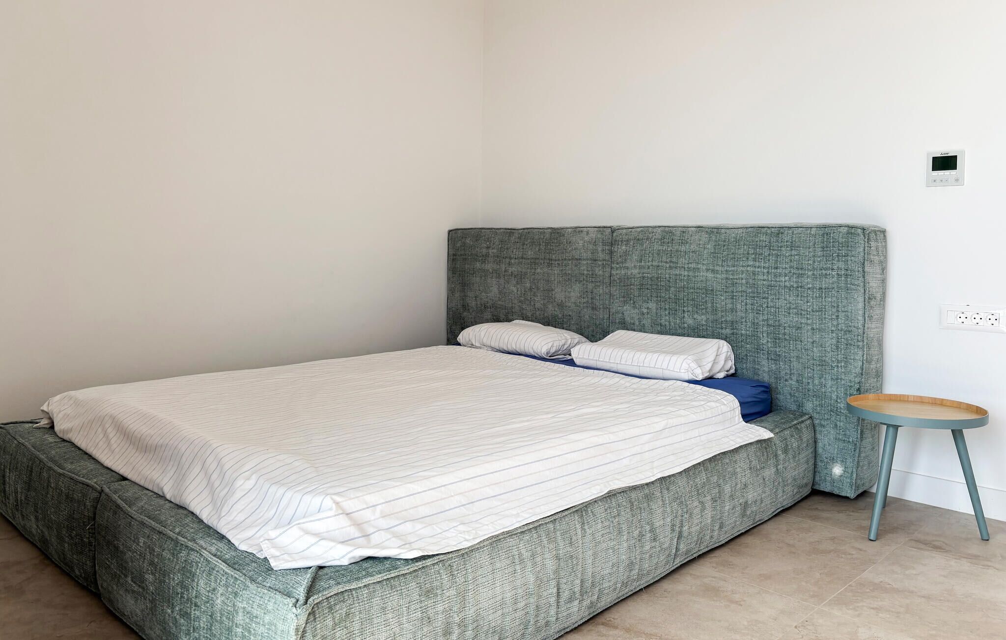 A bedroom with a bed, a small stool, and a wall socket.