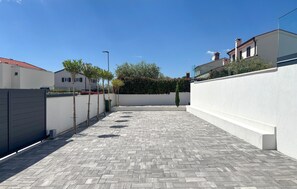 En asfalterad innergård med en vit vägg, ett metallstaket och en byggnad med ett rött tak i bakgrunden.