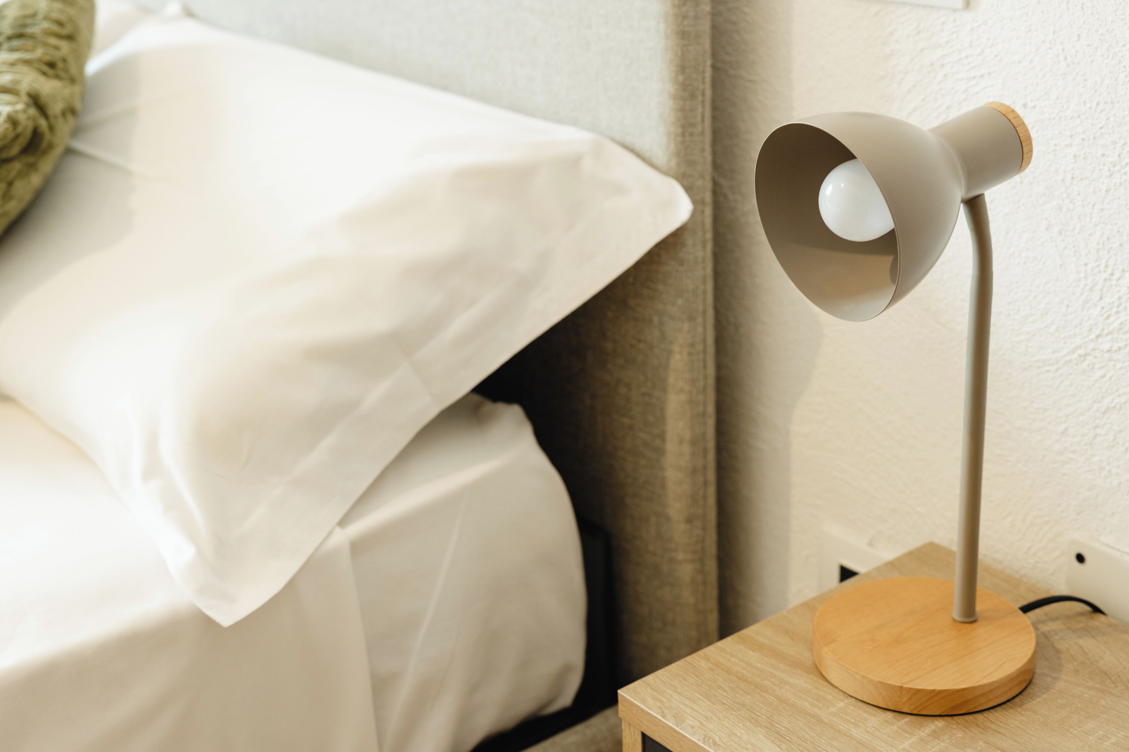 Un letto con lenzuola bianche, un comodino con una lampada e un poggiapiedi in legno.