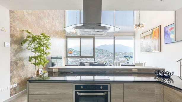 A modern kitchen with a large island, built-in oven, and a view of a cityscape through large windows. - Micrópolis (Monterrey)