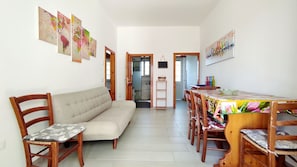 Un salon avec un canapé, des chaises en bois, une table à manger avec des chaises, et une cuisine en arrière-plan.
