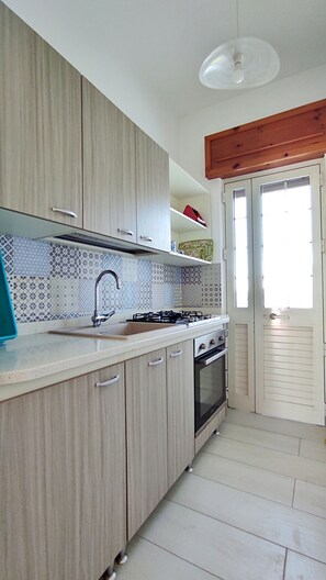 Une cuisine avec des meubles de rangement en bois, une cuisinière à gaz, un évier et une fenêtre.