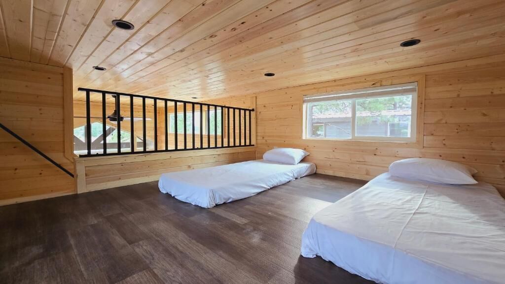 Une cabine avec deux lits, une fenêtre, un plafond en bois et une rambarde.
