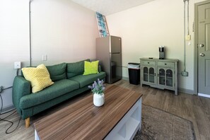 A compact living space with a green sofa, a wooden coffee table, a refrigerator, a cabinet, and a door.