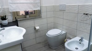 A bathroom with a toilet, bidet, sink, and window with a curtain. - Triple Economy Room (Catania)