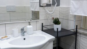 A bathroom with a white sink, a hairdryer, a potted plant, and a mirror. - Triple Economy Room (Catania)