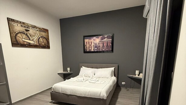A modern bedroom with a bed, a round rug, a wall-mounted light, and two wall art pieces. - Triple Economy Room (Catania)