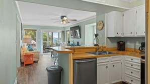 A kitchen with white cabinets, a refrigerator, a sink, and a ceiling fan. - Pelican's Landing 118- 3BR/2.5BA- Outdoor Pool (Myrtle Beach)