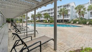 A covered outdoor pool area with lounge chairs and a building in the background. - Pelican's Landing 118- 3BR/2.5BA- Outdoor Pool (Myrtle Beach)