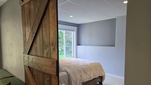 Un dormitorio con una cama, un separador de madera, un ventanal y un televisor montado en la pared.
