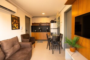 A modern living room with a brown sofa, dining table with chairs, a TV, and a kitchen in the background. - At Self #306 - Apartment in Manaira by Carpediem (João Pessoa)