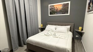 Una cama bien hecha con sábanas blancas, un cabecero gris y un cuadro en la pared.