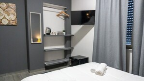 Una habitación de hotel con cama, televisión montada en la pared, un escritorio pequeño y estante con planta.