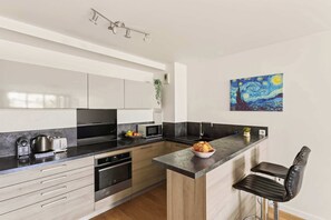 A modern kitchen with a central island, built-in appliances, and a painting on the wall. - Bright & Comfortable 2BR near Le Marais - Paris 11 (Paris)