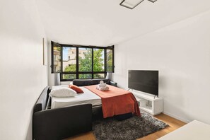 A modern bedroom with a bed, a TV, and a window with a view of buildings and trees. - Bright & Comfortable 2BR near Le Marais - Paris 11 (Paris)