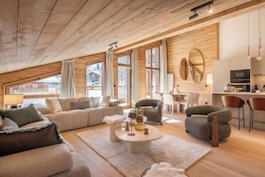 Ein gemütliches Wohnzimmer mit Holzboden, einer Couch, Sesseln, einem Couchtisch und einem Essbereich mit Tisch und Stühlen.