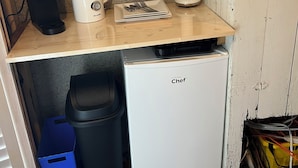 Une petite cuisine équipée d’une machine à café, d’un cuiseur à riz, d’une assiette avec des couverts, d’une poubelle et d’un petit réfrigérateur.