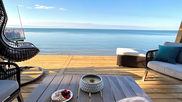 Une terrasse en bois avec vue sur la mer, une table avec une assiette de fruits rouges et une bougie, et une tasse verte.