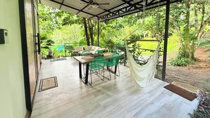 Eine Terrasse im Freien mit Tisch und Stühlen, einer Hängematte und Blick auf üppiges Grün.