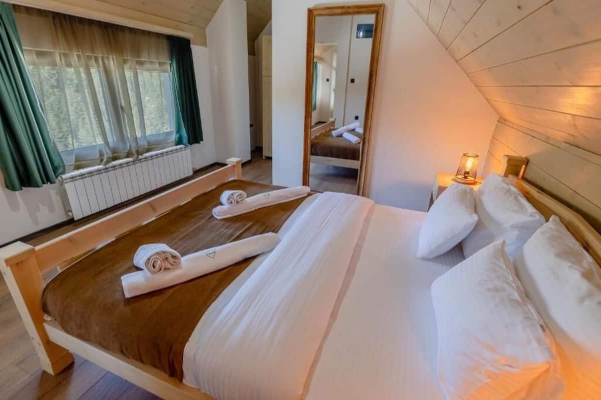 Une chambre à coucher avec un lit en bois, une fenêtre avec des rideaux, un radiateur et une table de chevet avec une lampe.