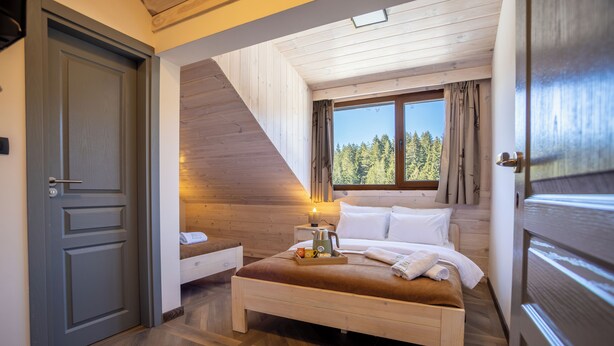 Un dormitorio con cama, mesita de noche, ventana con vistas a árboles y puerta.