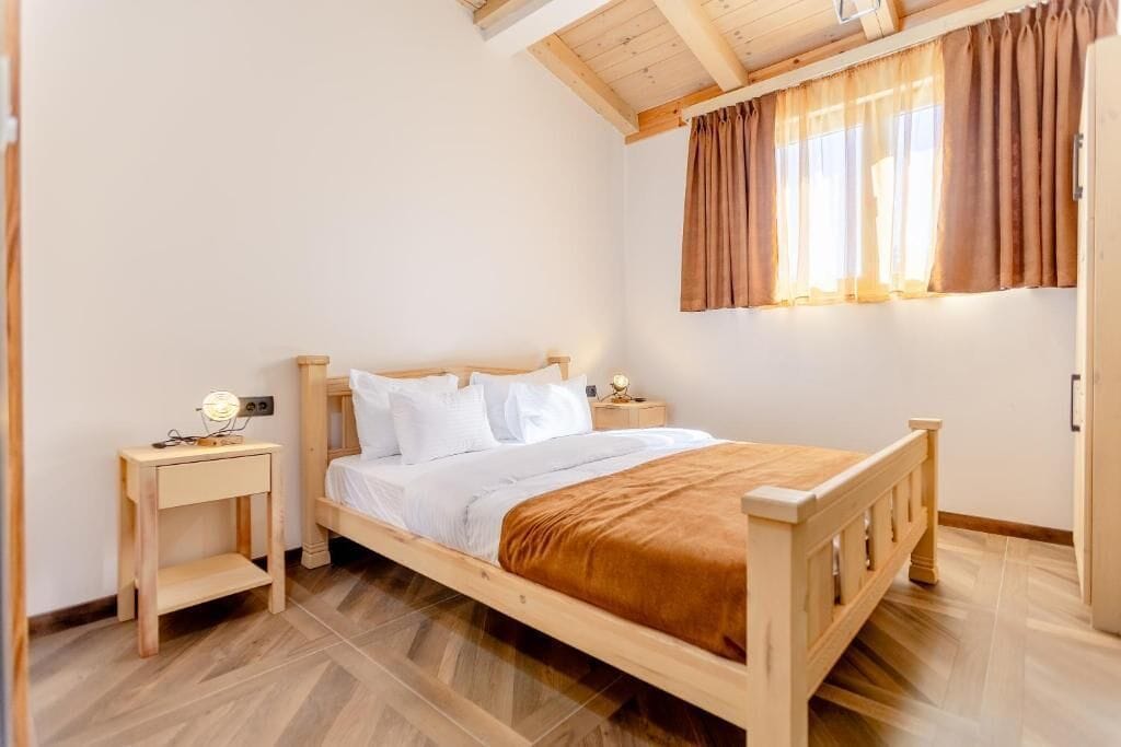 Un lit en bois avec une literie blanche, une table de chevet avec une lampe et une fenêtre avec des rideaux.