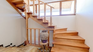 Una escalera de madera con barandilla de madera, un jarrón grande sobre un taburete pequeño, y una ventana sobre la escalera.
