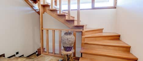 A wooden staircase with a wooden railing, a large vase on a small stool, and a window above the stairs.