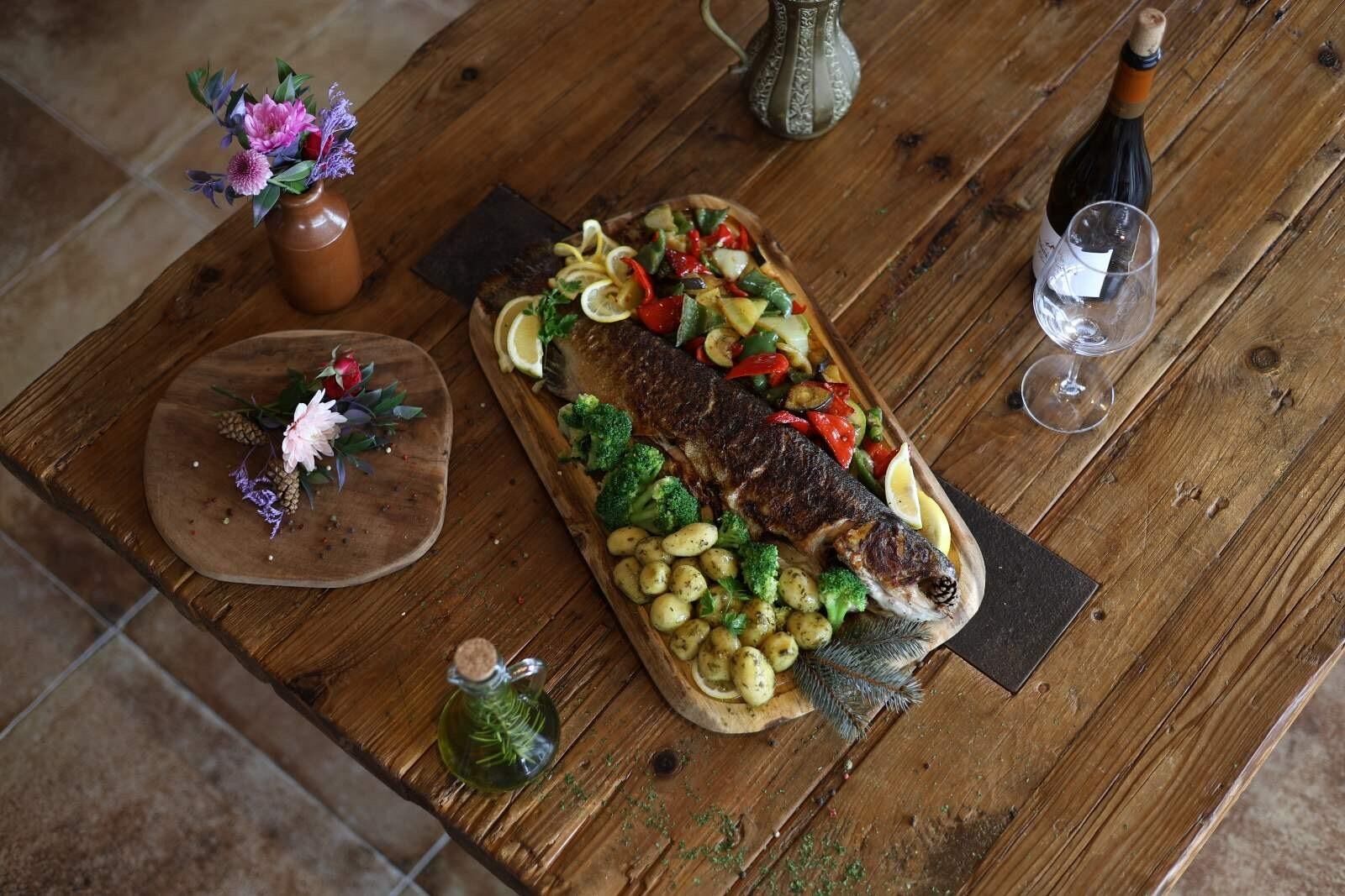 Un tavolo di legno con del pesce, verdure e una bottiglia di vino.