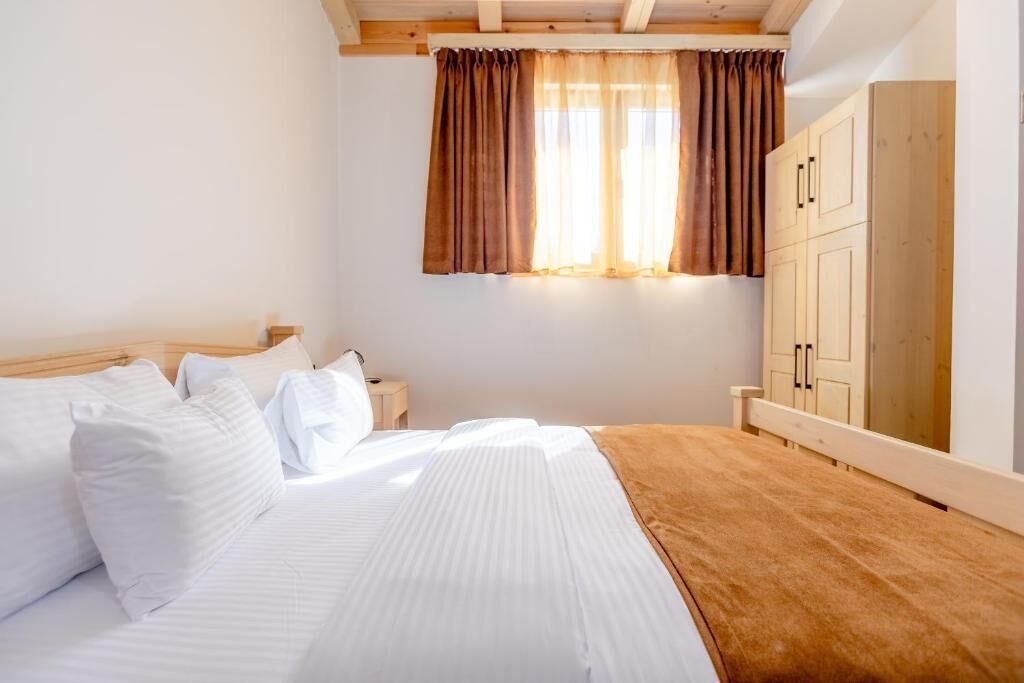 A bedroom with a bed, wooden headboard, a nightstand, a wardrobe, and a window with curtains.