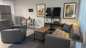 A living room with a sofa, armchair, coffee table, TV, and framed posters on the wall. - EC Taylor Coach House. Cozy 1-bedroom coach house in lovely New Carlisle,Indiana (New Carlisle)