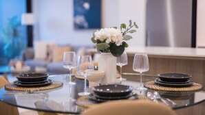 Uma mesa de jantar com pratos pretos, copos de vidro transparente, um vaso branco com flores e jogos americanos trançados.