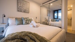 Quarto de hotel moderno com uma cama grande, um espelho, um quadro e vista para a cidade.