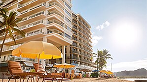 Ein Strandhotel mit mehreren Balkonen, Sonnenschirmen und Liegestühlen.