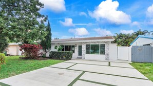A residential house with a front yard, a driveway, and a garage. - Remodeled Mid-century home with pool, hot tub & EV charger (Wilton Manors)