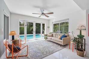 A spacious living area with a sofa, a chair, a ceiling fan, and a view of a swimming pool. - Remodeled Mid-century home with pool, hot tub & EV charger (Wilton Manors)